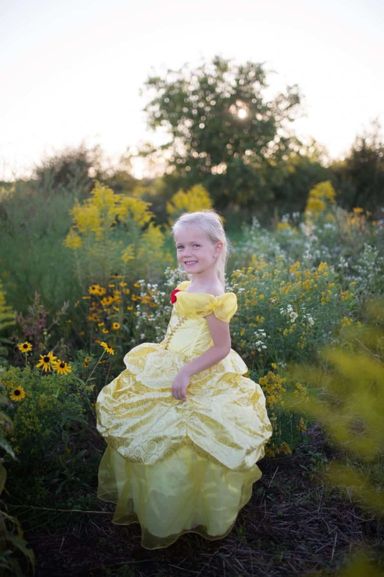 Meisje draagt een gele prinsessenjurk Belle met grote rok en off-shoulder mouwen in een bloeiende tuin