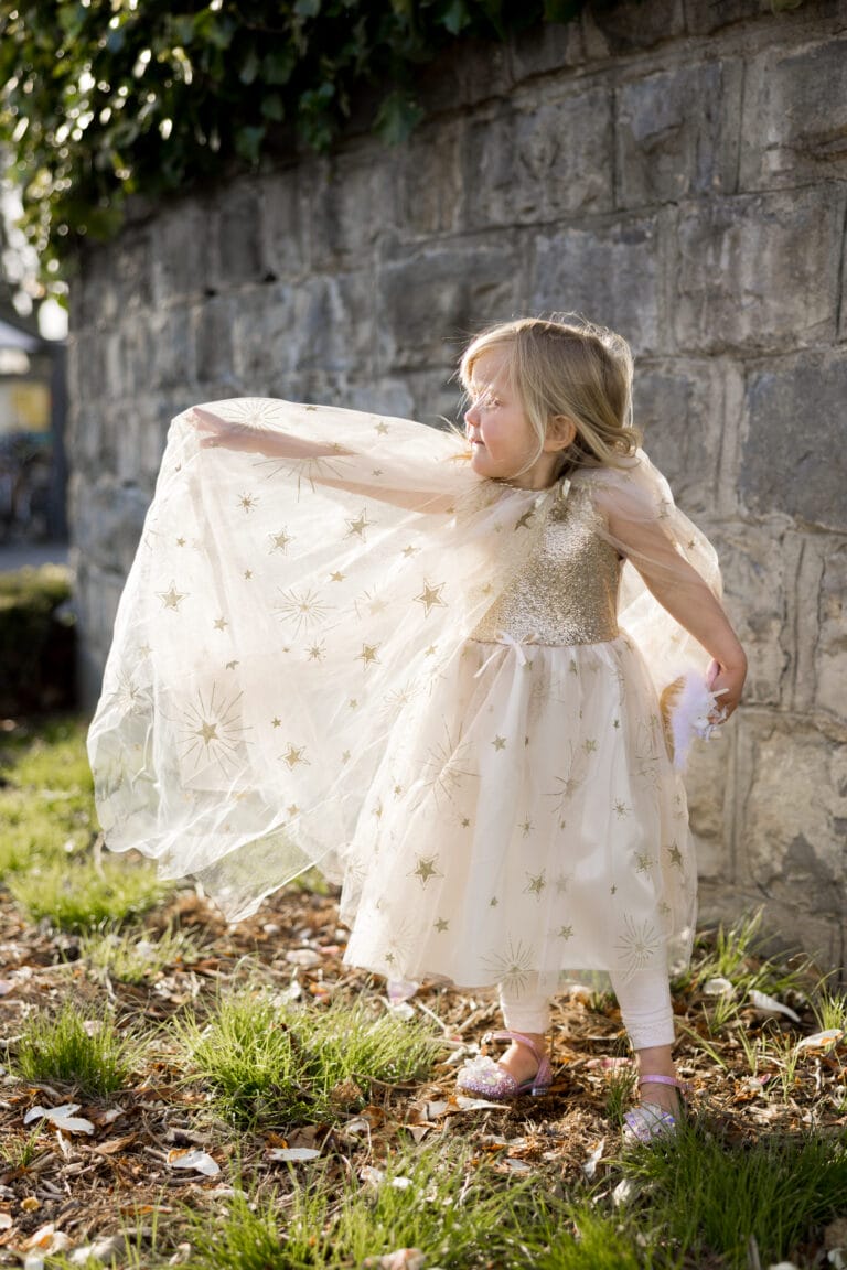 Meisje draagt de Golden Glam-cape, uitgespreid als een vleugel en versierd met gouden sterren.