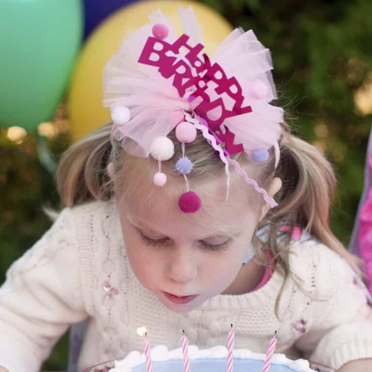 Roze happy birthday diadeem van Great Pretenders met tule, pompons en hangende linten op het hoofd van een meisje