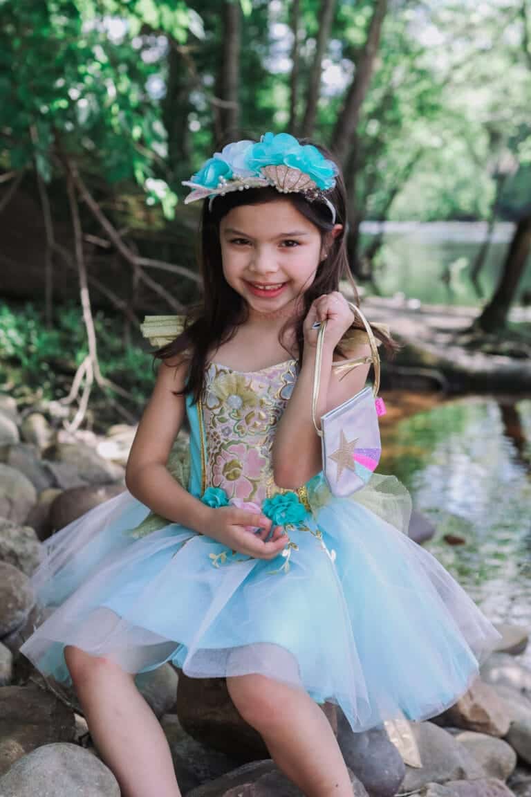 Meisje draagt de turquoise Zeemeermin haarband met bloemen en schelp, zittend bij het water in het bos