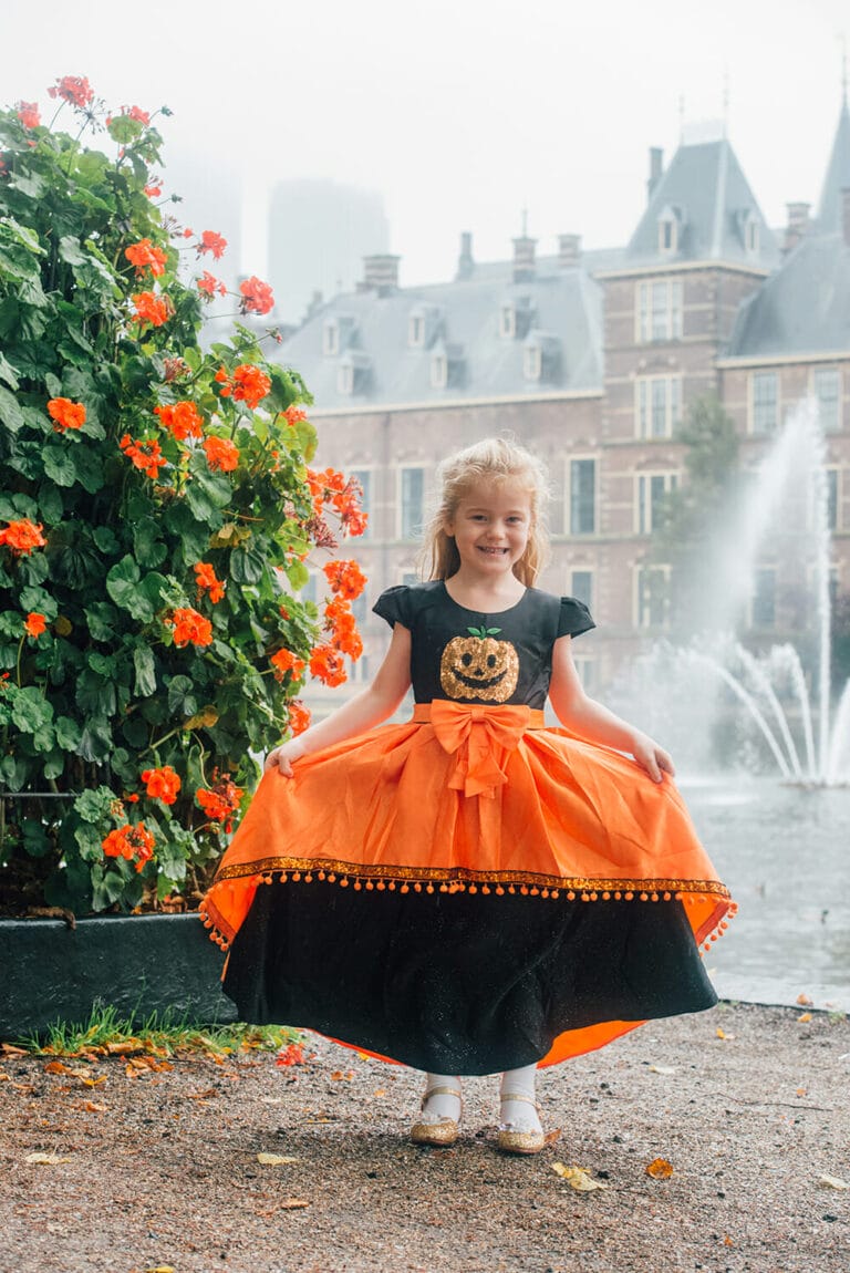 Meisje draagt een oranje en zwart halloweenkostuum met pompoen op de jurk en grote strik
