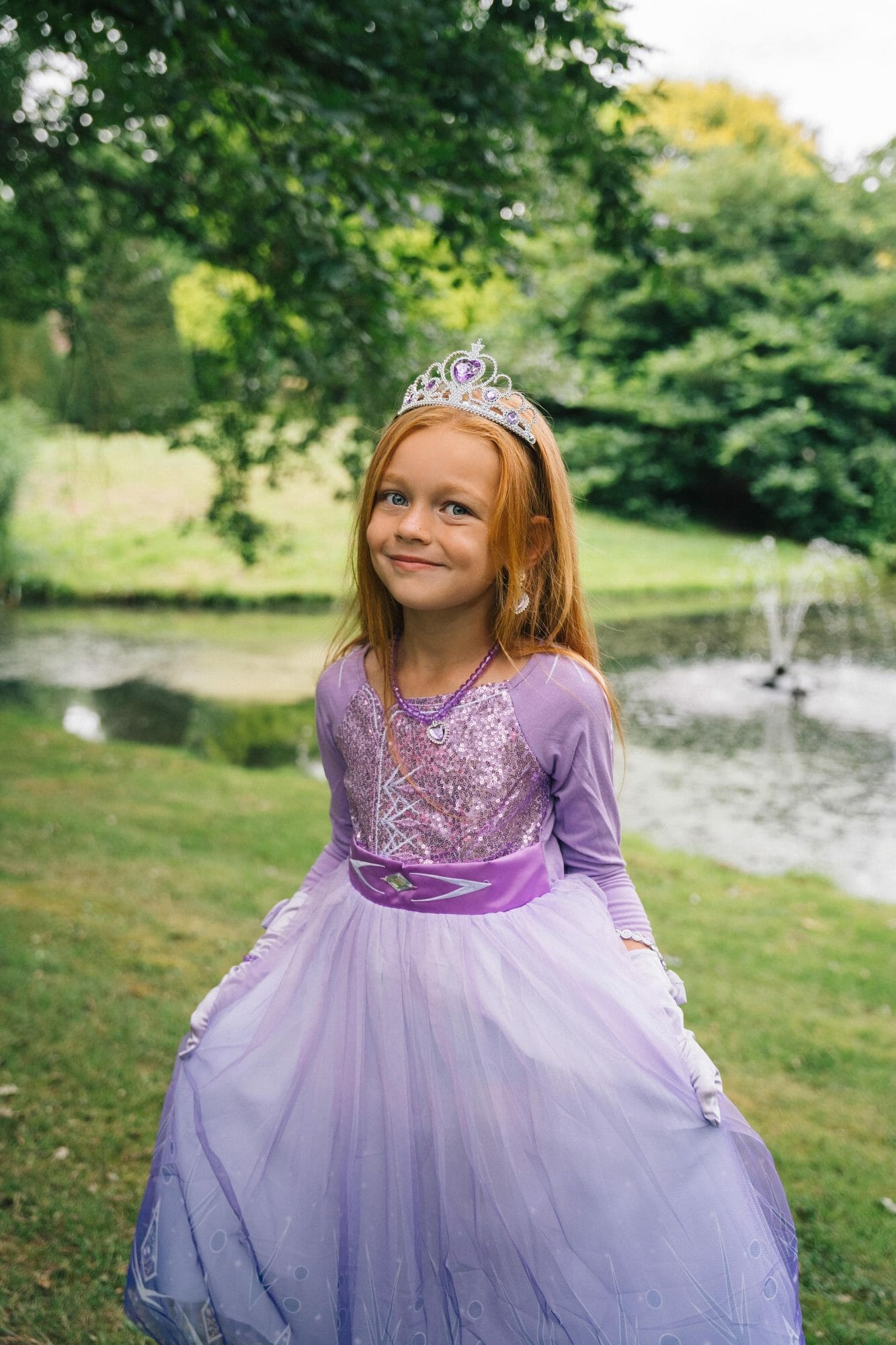 Meisje draagt een paarse Elsa jurk met glinsterend lijfje, tiara en wijde tule rok bij een vijver