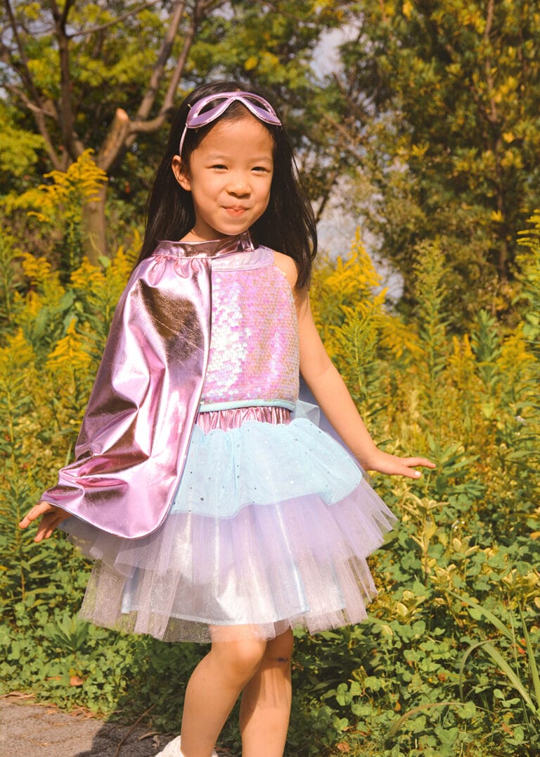 Een kind draagt de Great Pretenders roze superheld verkleedset met glanzende cape, tule tutu en roze oogmasker in het groen.