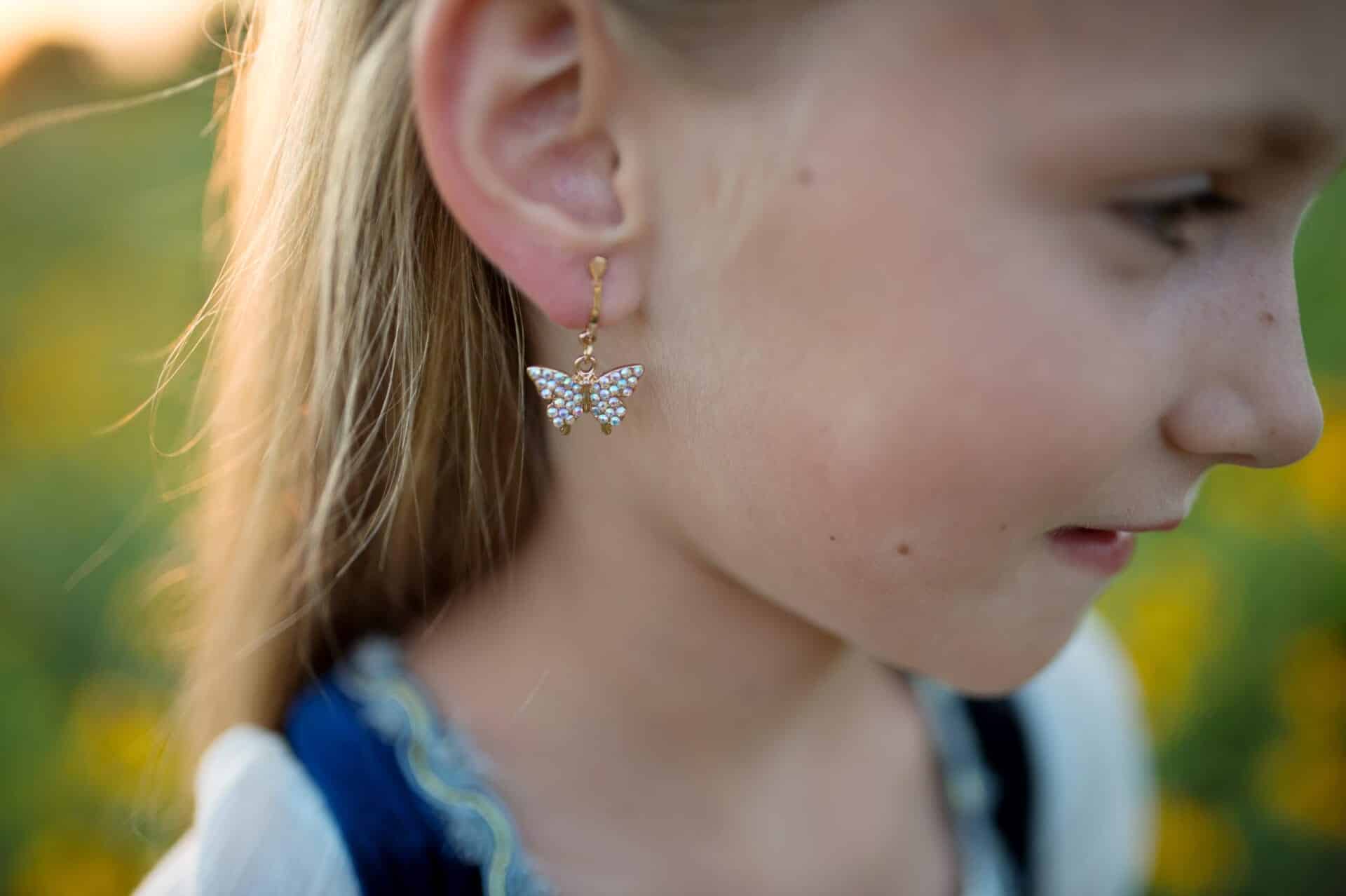 Close-up van een meisje buiten met een vlinder oorbel met fonkelende steentjes, zichtbaar aan haar oor in zijaanzicht.