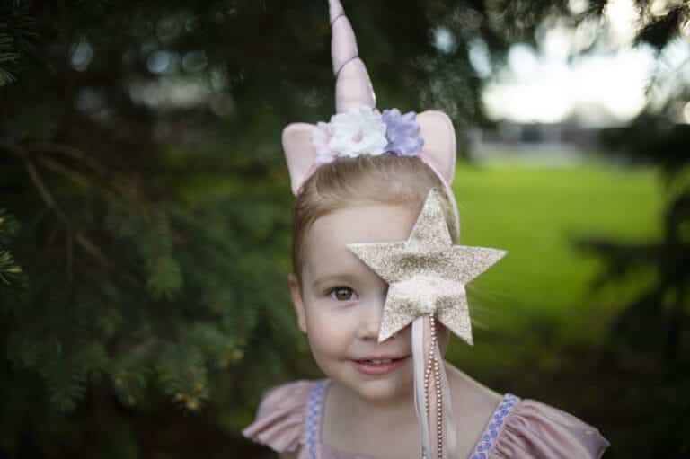 Meisje houdt de gouden glitter prinsessen toverstaf van Great Pretenders voor haar gezicht, met linten en parelkettinkje