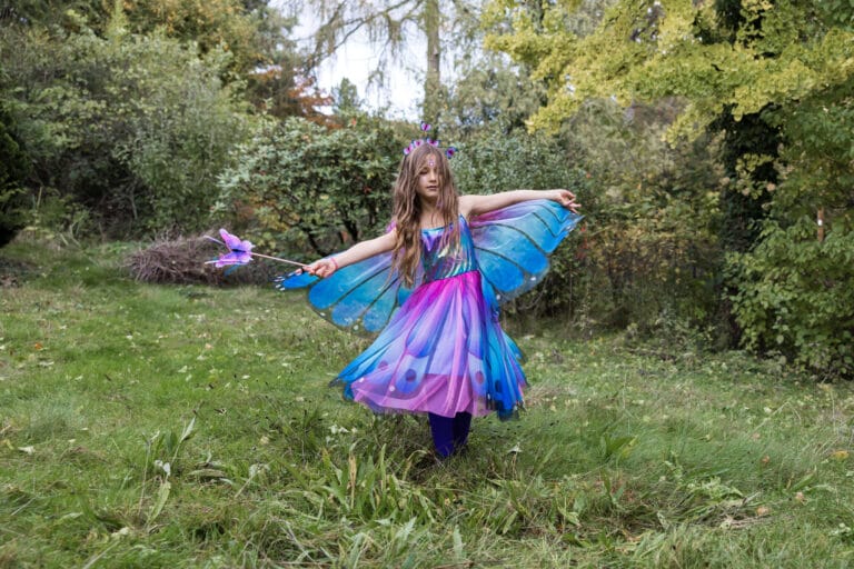 Meisje houdt de Great Pretenders vlindertoverstaf met paarse en roze vlinder vast in een groene tuin.