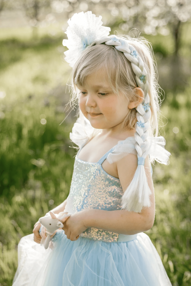 Meisje draagt een Great Pretenders Elsa haarvlecht met witte en blauwe sneeuwvlokken naast een lichtblauwe jurk