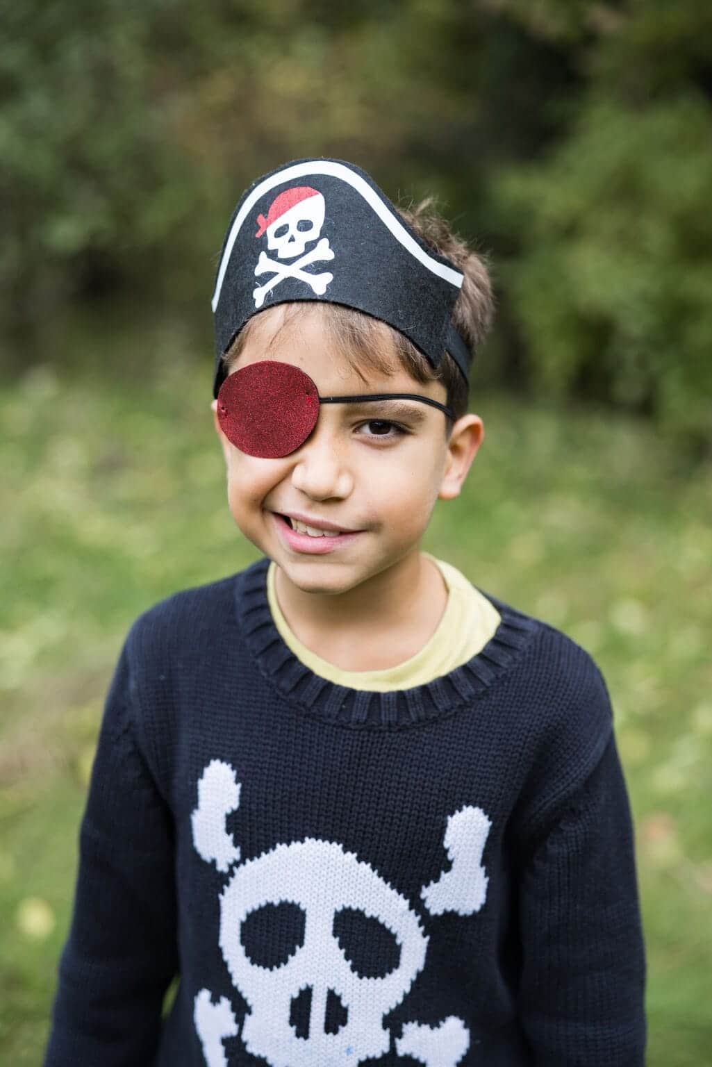 Jongen draagt een zwarte piratenhoed als hoofdband met rood ooglapje, met een witte schedel en gekruiste botten
