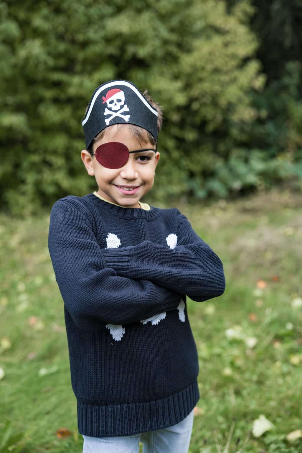 Jongen draagt een zwarte piratenhoed als hoofdband met rood ooglapje, buiten tussen het groen
