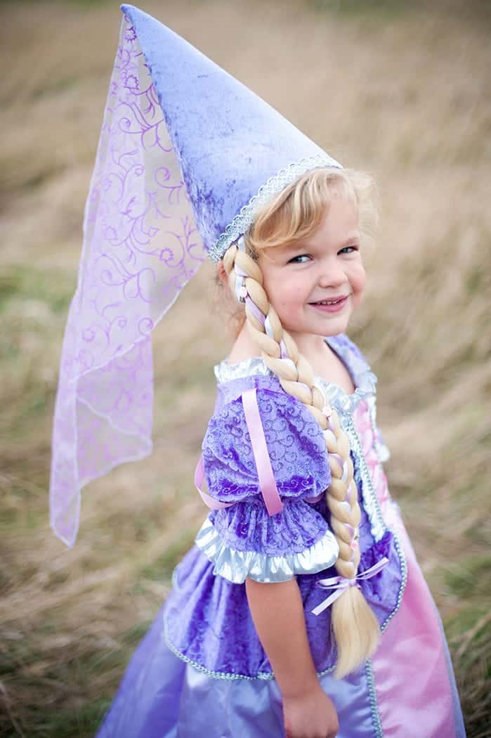 Meisje draagt de paarse Great Pretenders prinsessenhoed met lange blonde vlecht, passend bij haar paarse Rapunzeljurk.