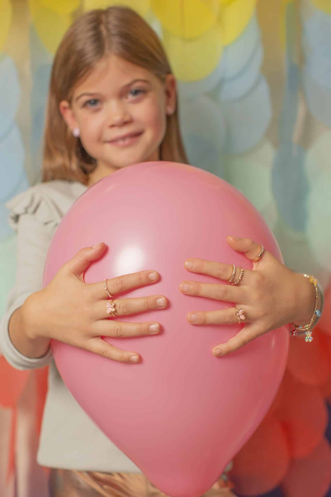Meisje houdt een roze ballon vast en draagt drie vlinderringen aan haar vingers