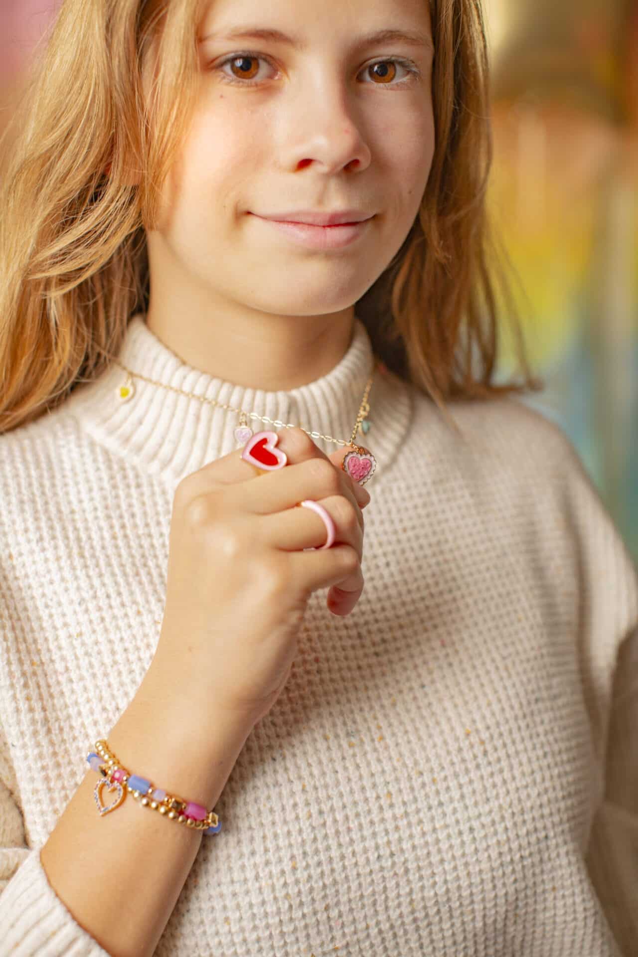 Meisje draagt een kinderring hartje uit de set kinderringen – 2 stuks, met een rood hartje en een roze ring om haar vingers.