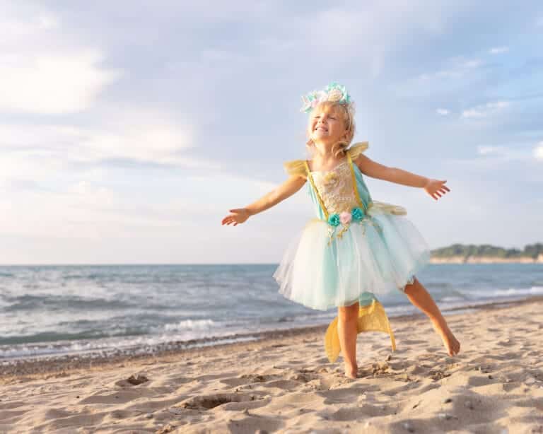 Meisje draagt een zeemeermin jurk met turquoise lijfje, witte tule rok en gele staart op het strand