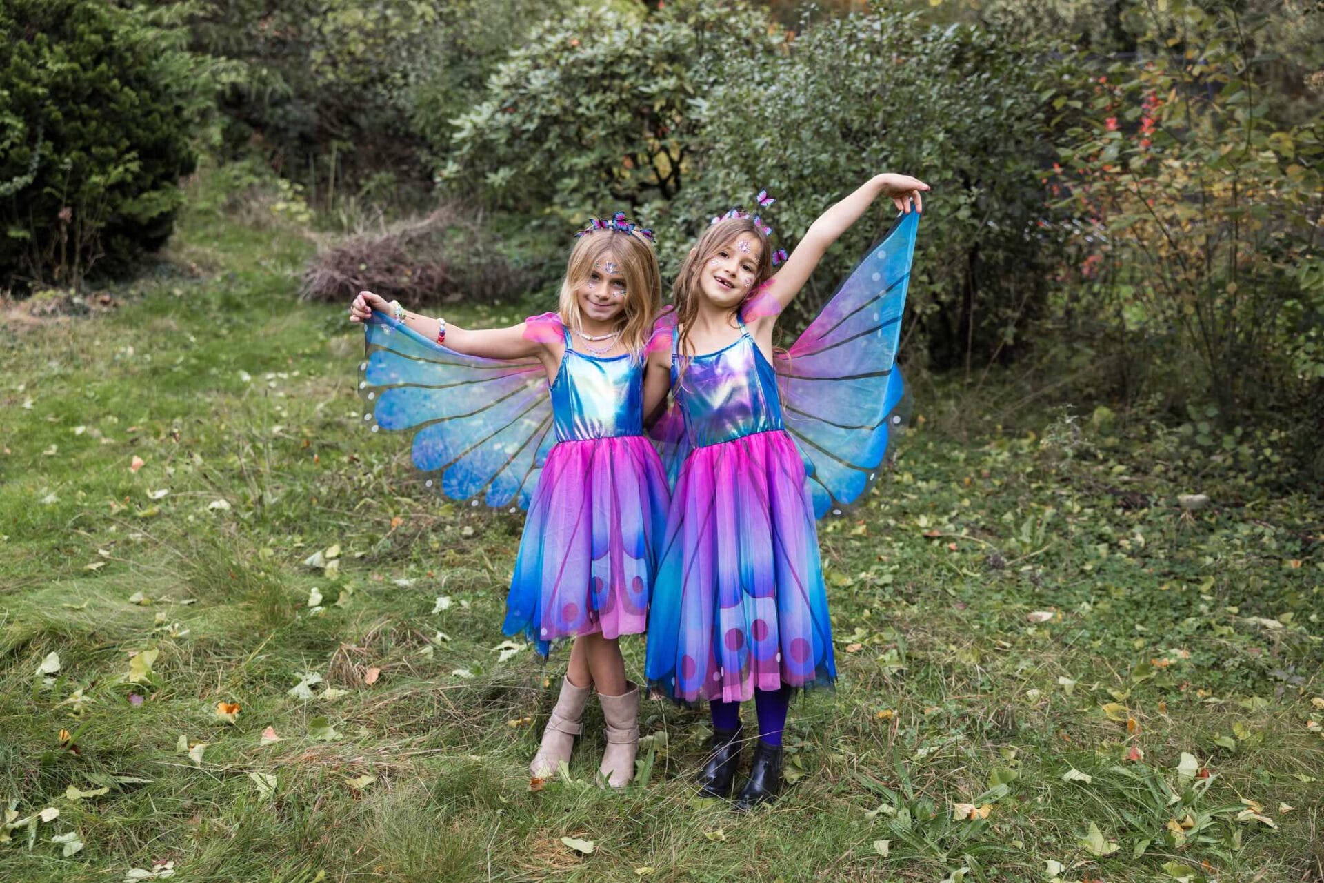 Twee meisjes dragen een blauw-paarse vlinderjurk met bijpassende vleugels in een bosrijke omgeving.