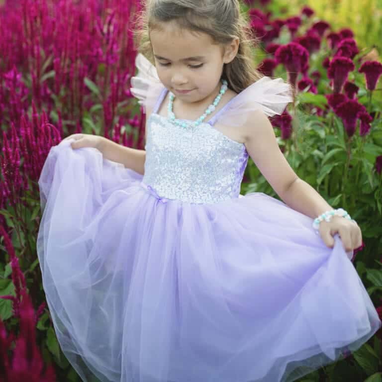 Meisje draagt een paarse prinsessenjurk met pailletten en houdt de wijde tule rok vast tussen bloemen