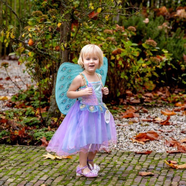 Meisje draagt een paarse elfenjurk met glinsterend lijfje, tule rok en turquoise pauwenvleugels in de tuin