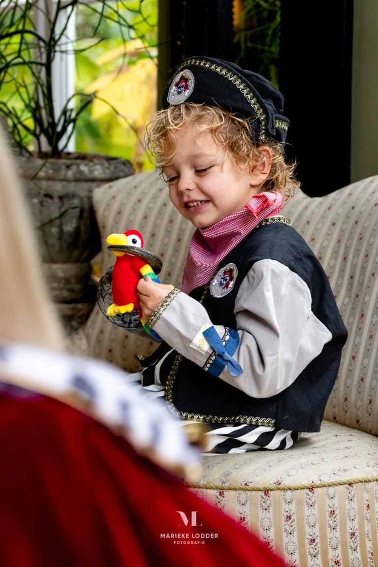 Piratenpak kind gedragen door een jongen, met zwart-witte mouwen, een piratenhoed en een kleurrijke pluche papegaai.
