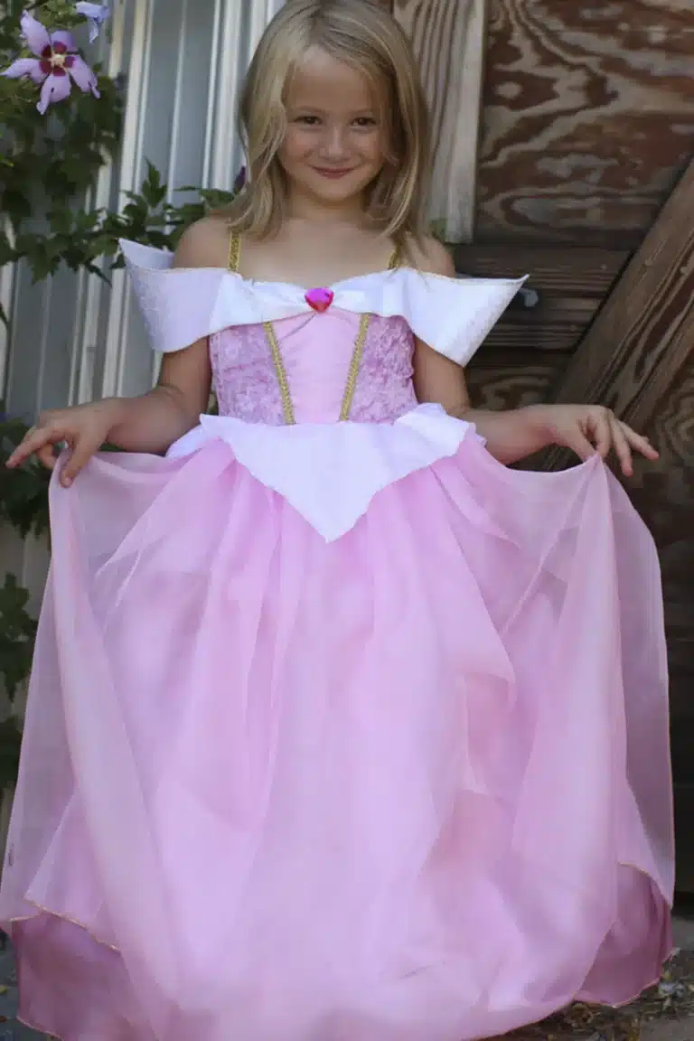 Meisje houdt de wijde roze rok van de Doornroosje Deluxe baljurk omhoog en toont de witte strik