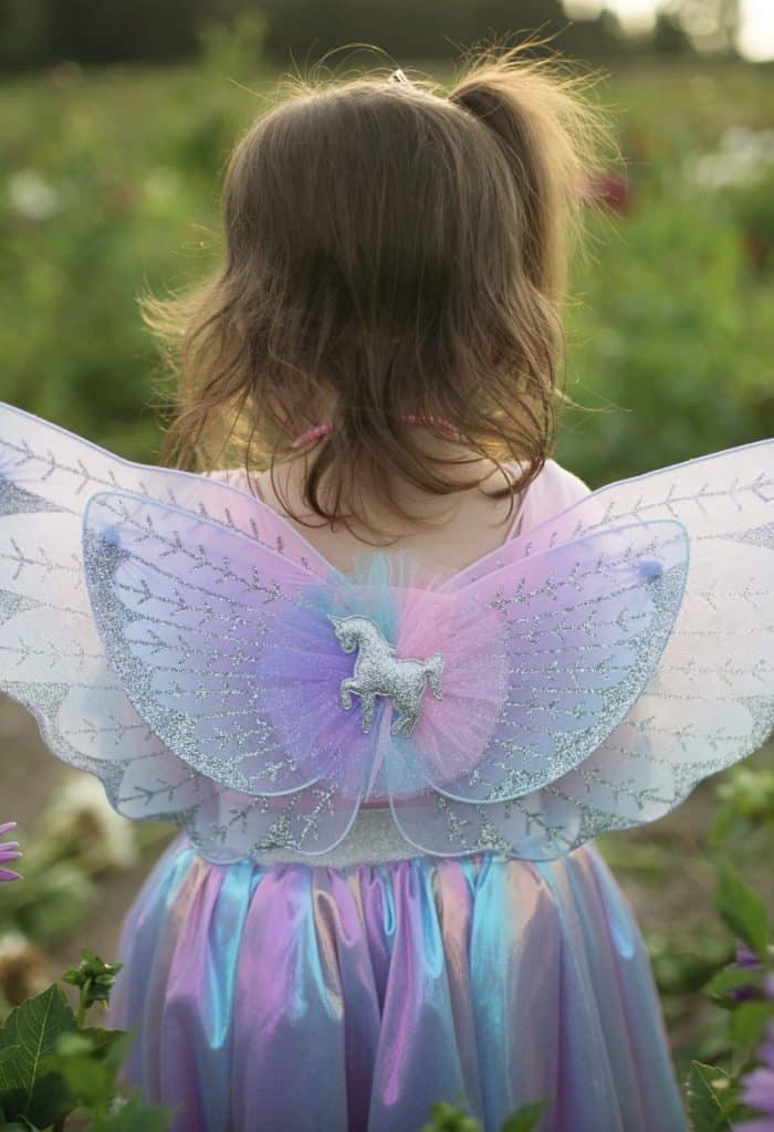 Kind draagt een unicorn jurk kind met pastelregenboogrok en brede glittervleugels, van achteren gezien.