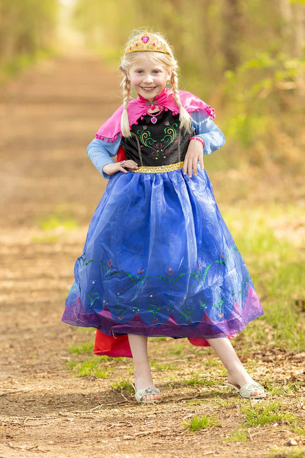 Een meisje draagt de Elsa jurk van Het Betere Merk met kroon en blauwe rok op een bospad.