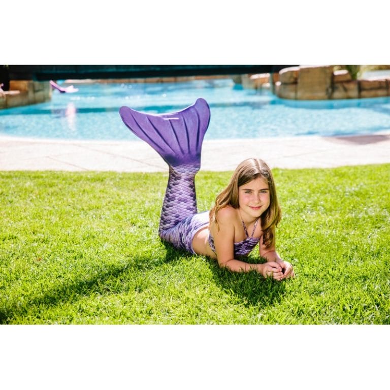 Meisje draagt de paarse Kuaki Mermaids-zeemeerminstaart met monovin en bikinitop op het gras bij een zwembad.