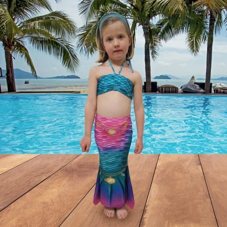 Meisje draagt een turquoise en roze zeemeerminstaart met bikinitop bij het zwembad; de staart heeft een brede vin.
