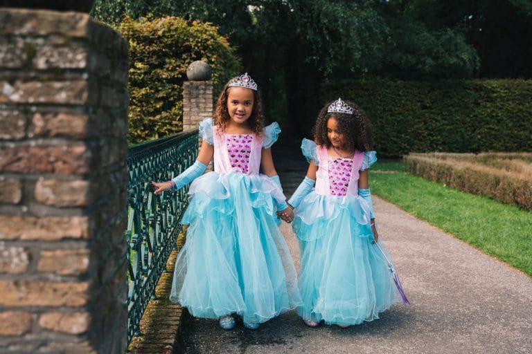 Twee meisjes dragen een blauwe Elsa prinsessenjurk met roze lijfje, tule rok en tiara op een tuinpad
