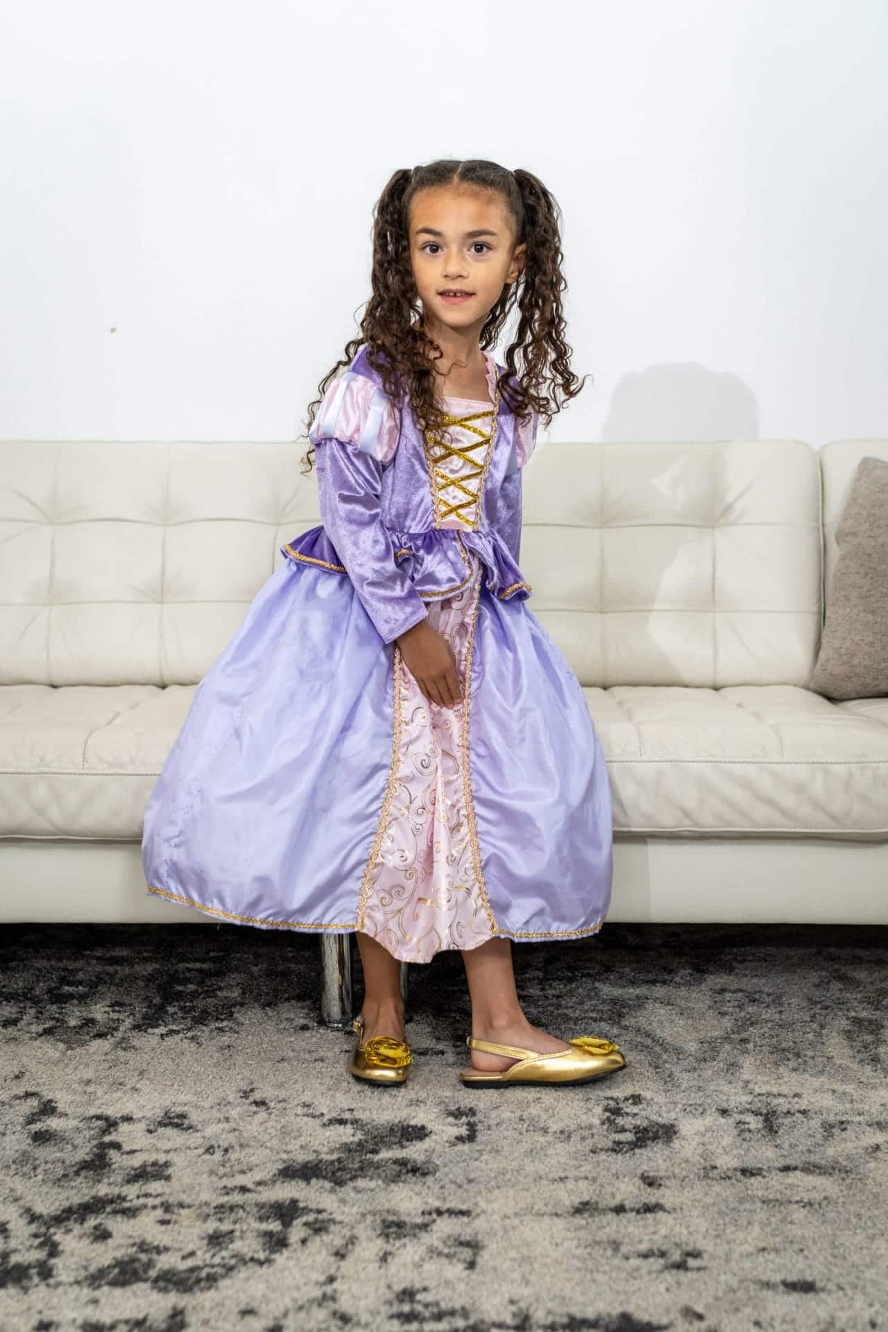 Gouden schoenen meisje met glitterrozetten, gedragen onder een paarse prinsessenjurk.