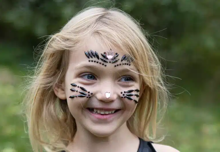 Een meisje draagt zwarte en roze kinderstickers als sierlijke gezichtversiering, met een hartje op haar neus.