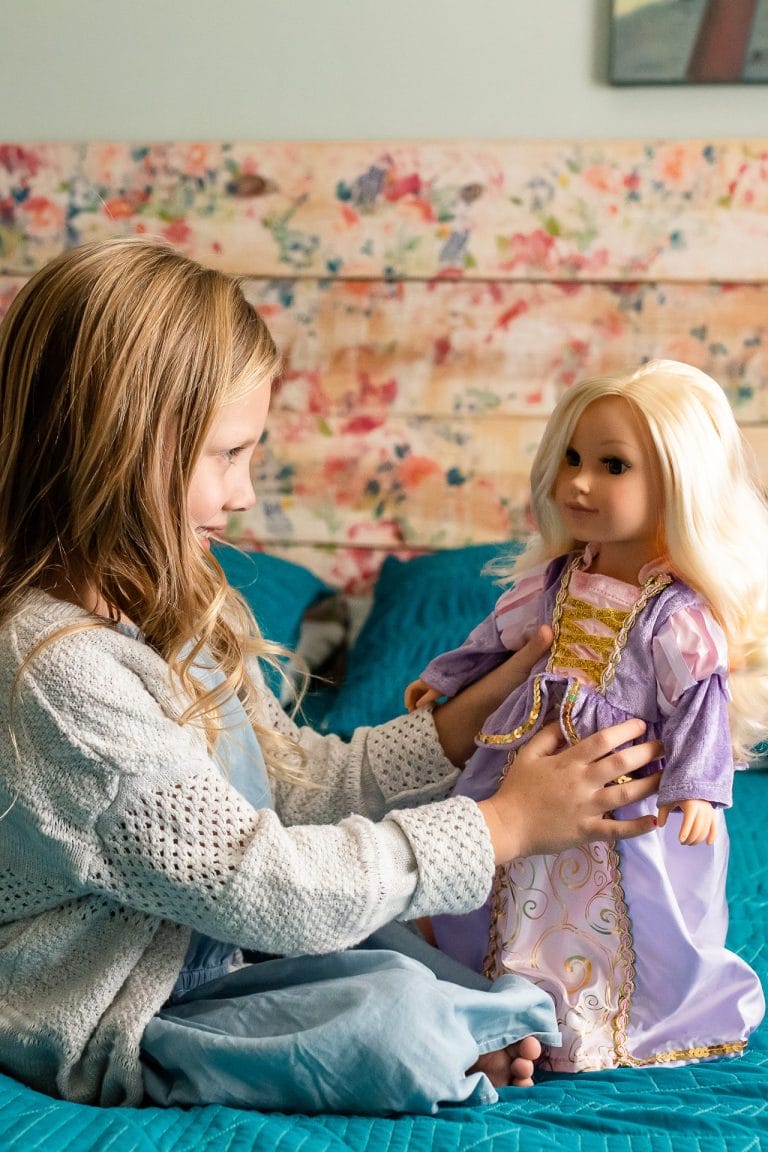 Meisje houdt een pop vast in een paarse poppenjurk met gouden versieringen en roze mouwen