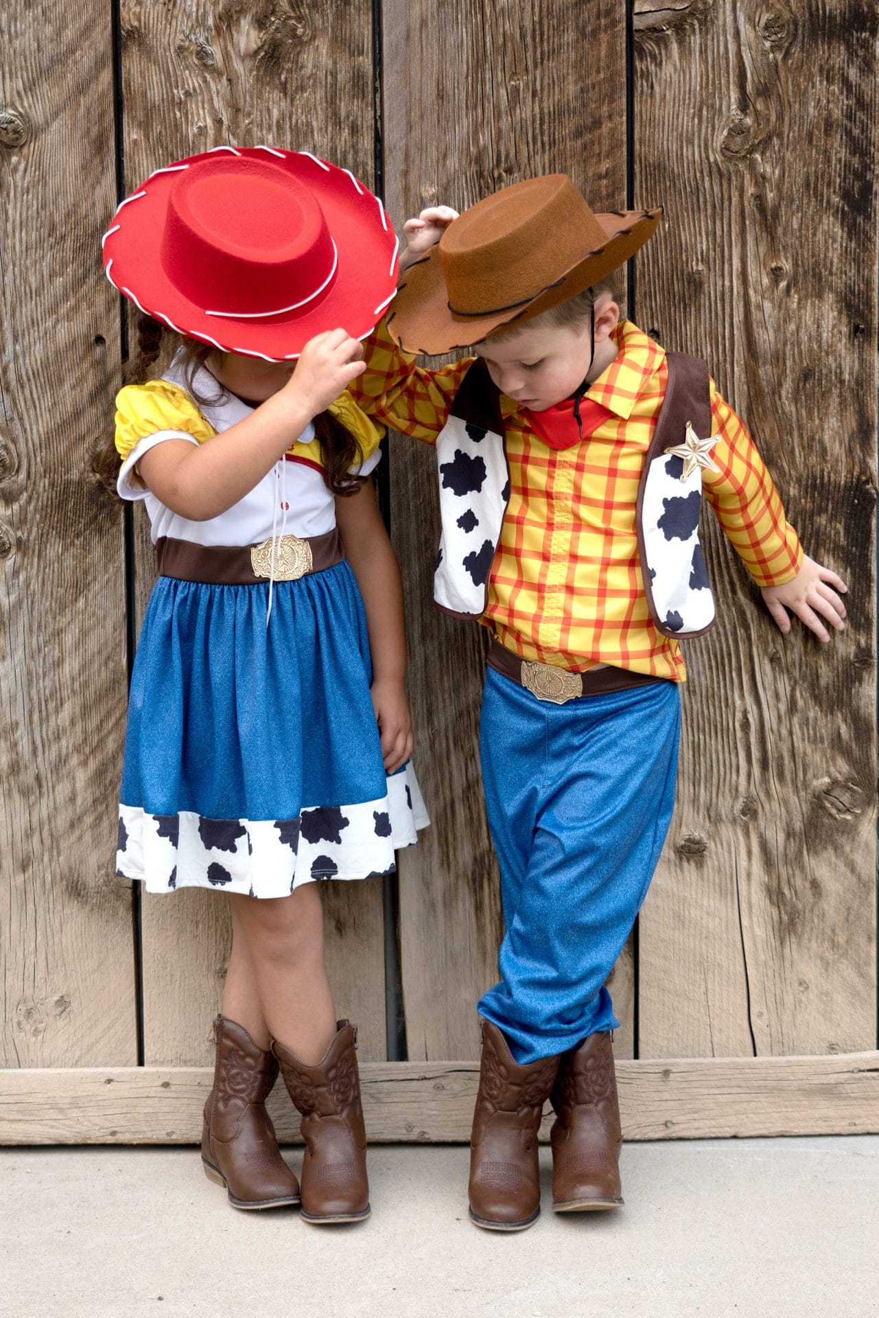 Jongen draagt een cowboy set met geel-rood geruit overhemd, koeienvest, blauwe broek en bruine cowboyhoed