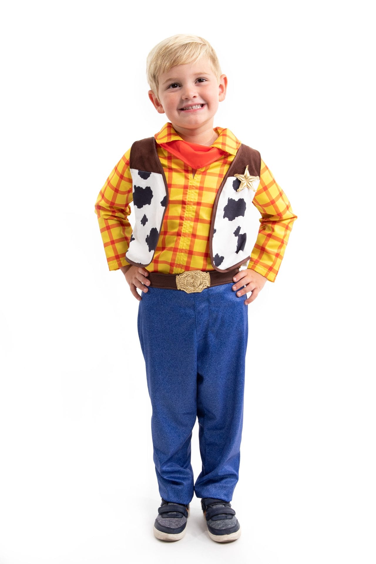 Jongen draagt een 4-delig cowboy set met geel-rood geruit overhemd, koeienvlekkenvest, rode halsdoek en blauwe broek.