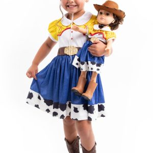 Vooraanzicht van een meisje in een Toy Story-cowgirljurk met koeienprint, dat een pop vasthoudt tegen een witte achtergrond.