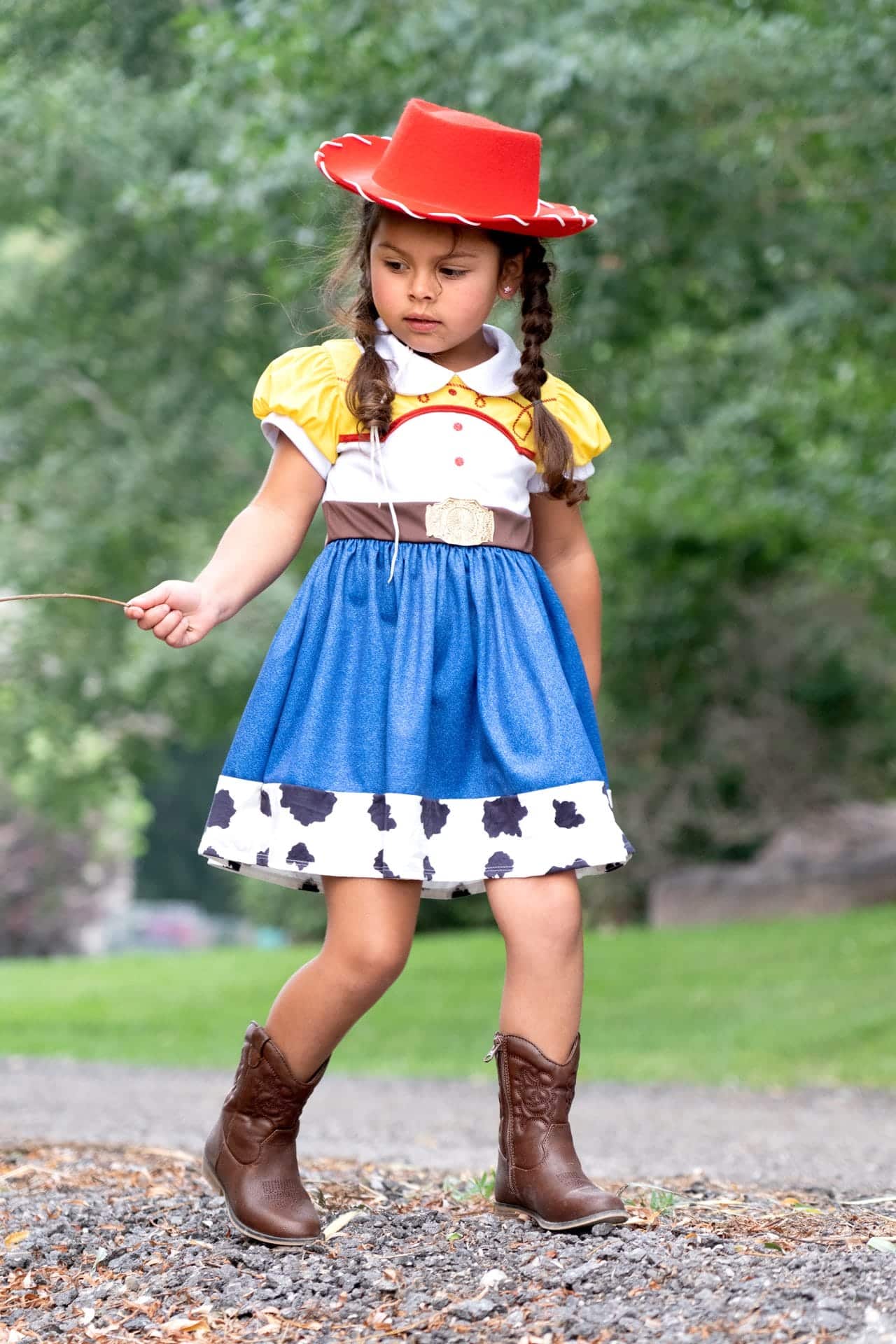 Meisje draagt de Toy Story-cowgirljurk met blauwe rok, koeienprint, bruine riem en rode cowboyhoed