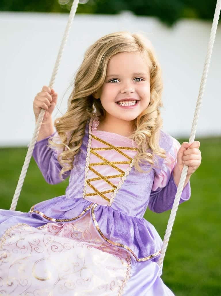 Meisje op een schommel draagt een paarse rapunzel prinsessenjurk Classic met roze mouwen en gouden veterdetails.