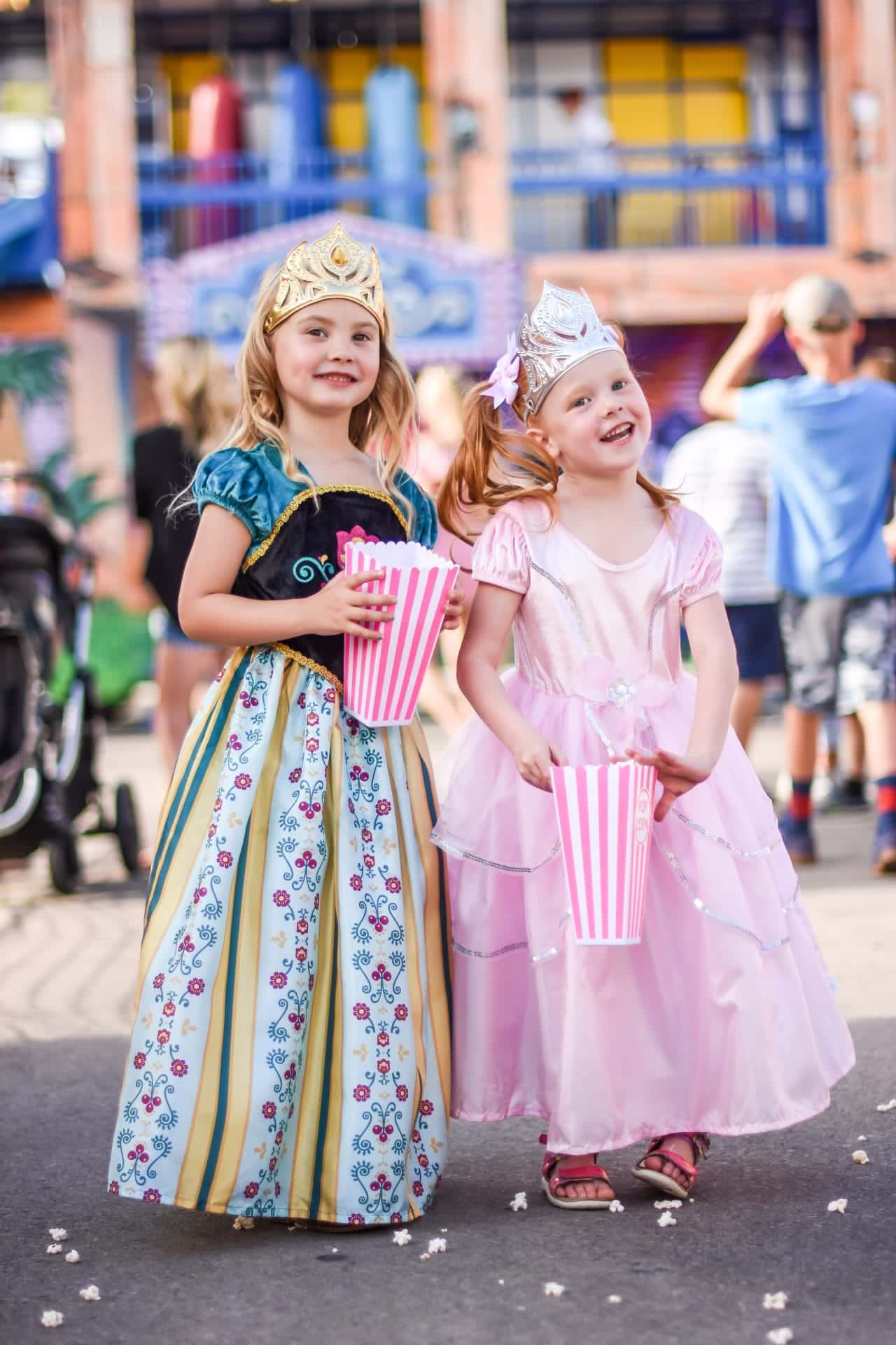 Meisje draagt de roze Royal Pink Princess-prinsessenjurk met zilveren details en een kroon, naast een meisje in een blauwe jurk.