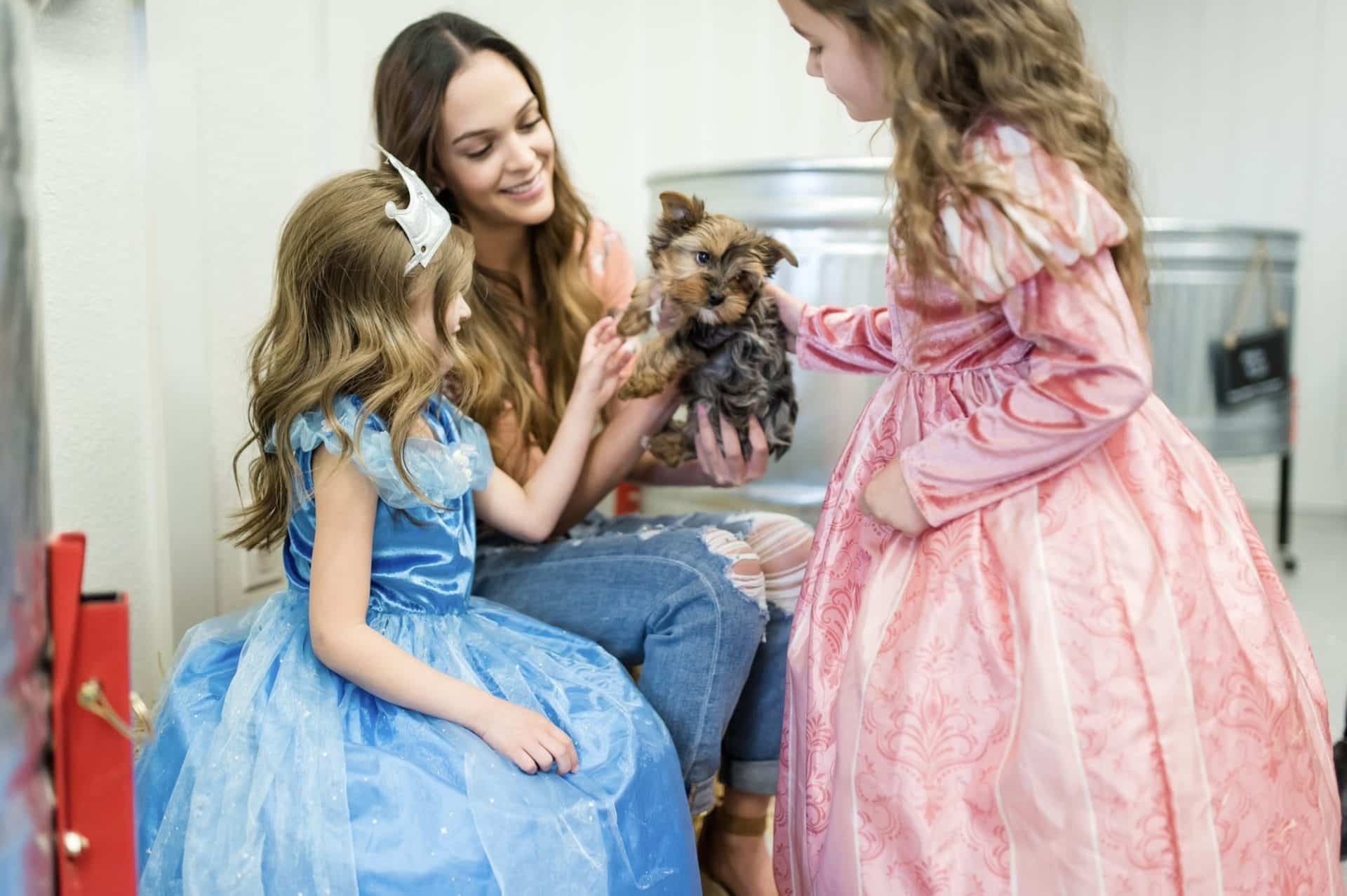 Meisje draagt een zilveren kroon van stof bij een blauwe prinsessenjurk, terwijl een ander meisje in roze toekijkt.