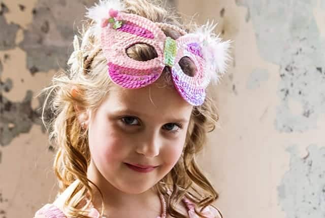 Meisje draagt een roze prinsessenmasker met witte veren, bloemen en glanzende versieringen.