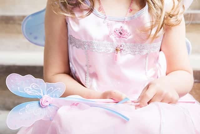Een meisje houdt een roze-blauwe prinsessentoverstaf met vlinderversiering boven haar roze prinsessenjurk.