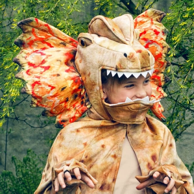 Kind draagt een bruine Dilophosaurus dino cape met dinosauruskop, tanden, vleugelkraag en klauwhanden.
