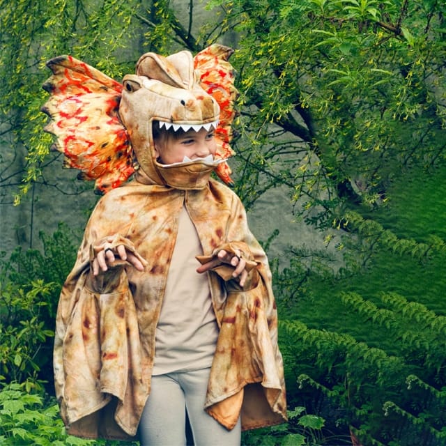 Kind draagt een bruine dinosaurus cape met capuchon met tanden, vleugelachtige kraag en mouwen met klauwen