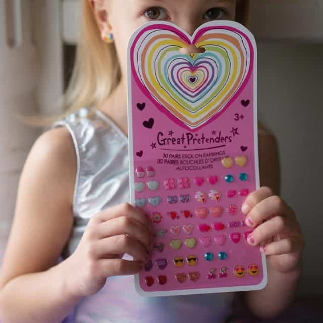 Een kind toont de Rainbow Heart plakoorbellen kind: 30 paar hartvormige oorstickers op een roze kaart.