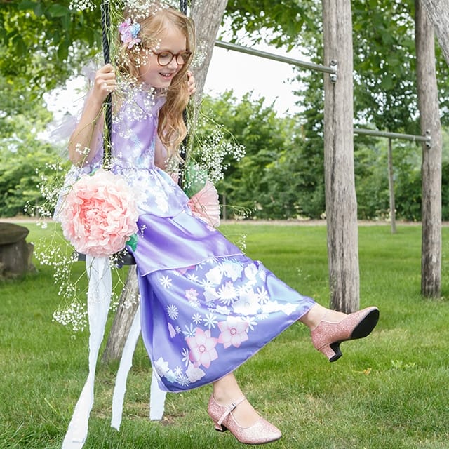 Meisje draagt een paarse encanto jurk met bloemenprint, zittend op een schommel met roze schoenen