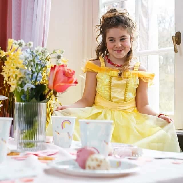 Meisje draagt een gele Belle jurk met glanzende details tijdens een feestelijk gedekte tafel.
