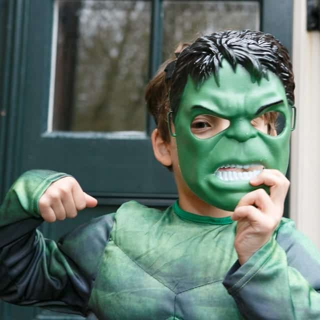 Jongen draagt een groen kunststof superheldenmasker met zwart haar en trekt een stoere gezichtsuitdrukking