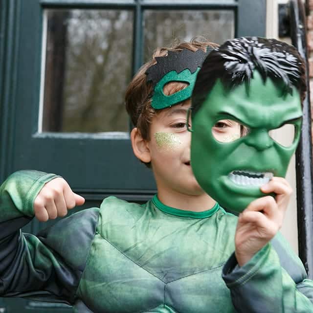 Jongen houdt een groen kunststof superheldenmasker voor zijn gezicht en draagt een groen superheldenkostuum