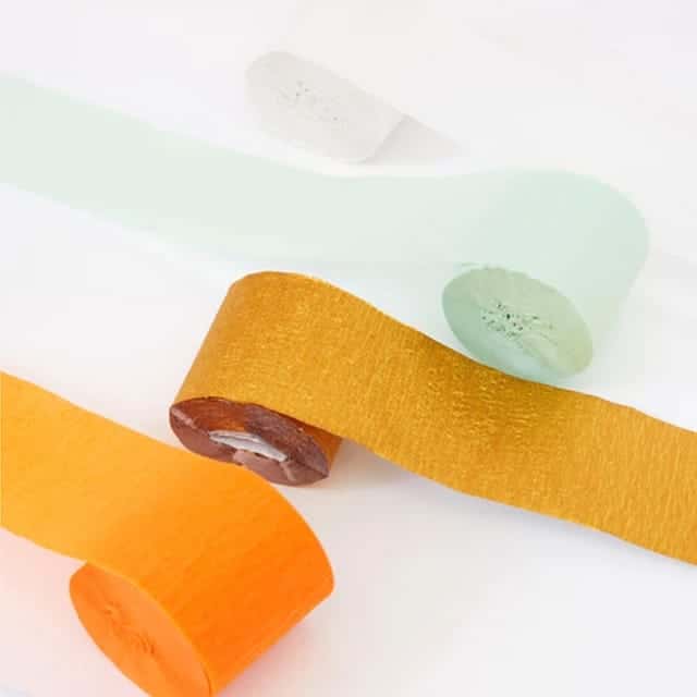 Detail van crepepapier oranje streamers op rol, met daarnaast goudgele en mintgroene crêpepapier streamers