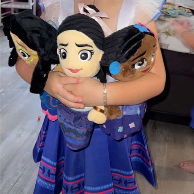 Kind houdt het Encanto Luipaard knuffeldier met bruine gevlekte vacht vast naast twee poppen.