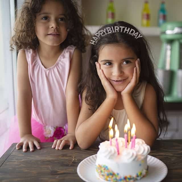 Meisje draagt het happy birthday diadeem van Great Pretenders tijdens een verjaardag, met een taart op de voorgrond.