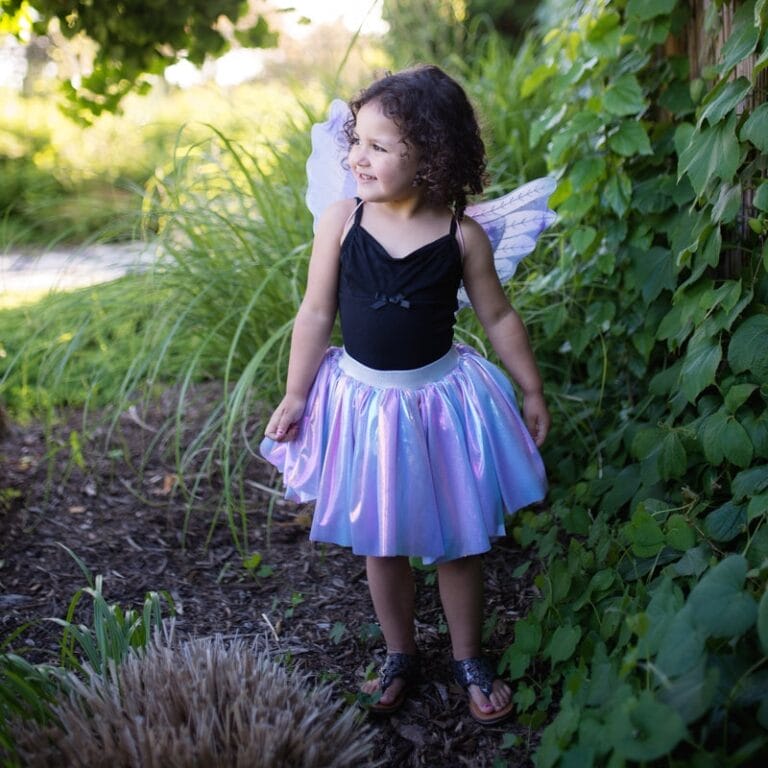 Kind draagt het Great Pretenders unicorn kostuum met glanzende paarse rok en glittervleugels in een tuin